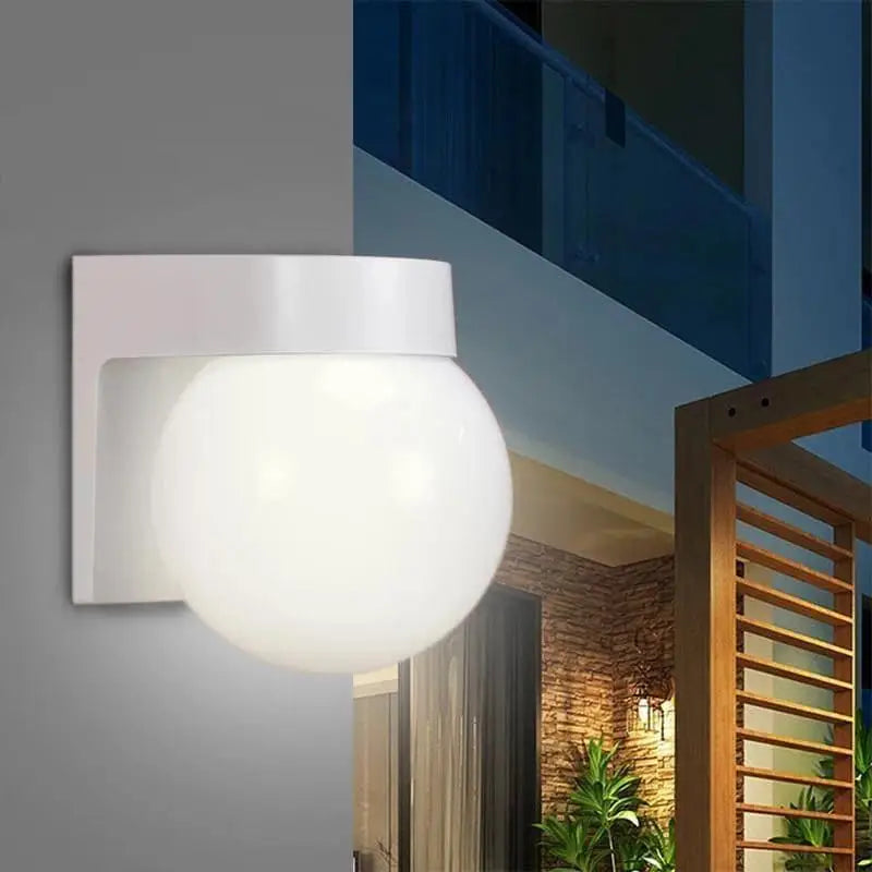 The Modern Globe Outdoor Acrylic Wall Light with white globe and square mount, illuminated at night.