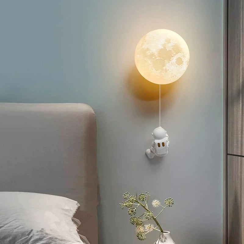 The Planet Design Glass Wall Light shaped like a moon with an astronaut figure hanging.