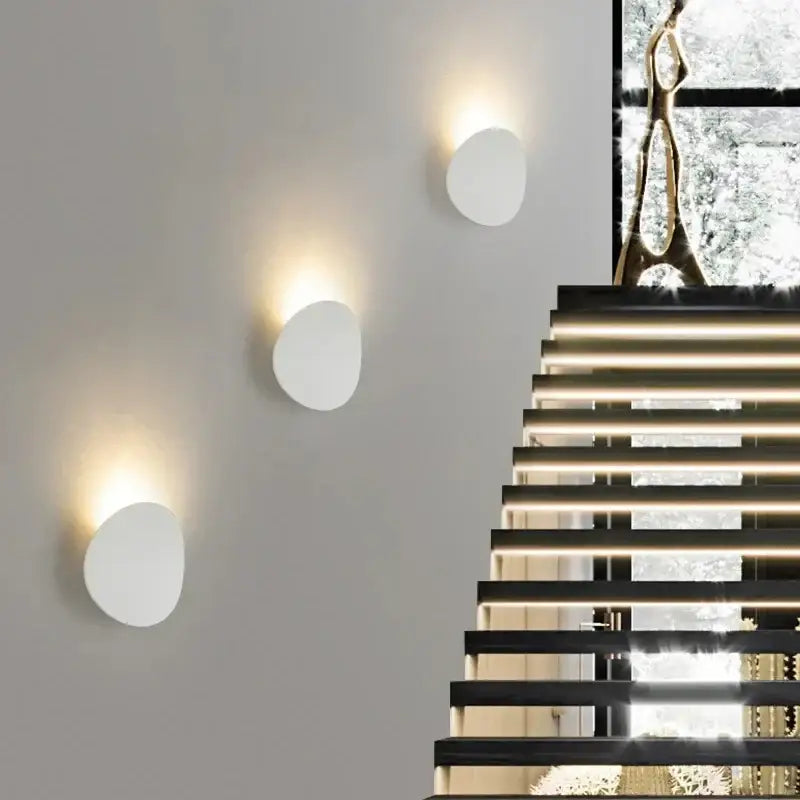 Three round aluminum LED wall lights emitting soft, warm light against a modern wall.