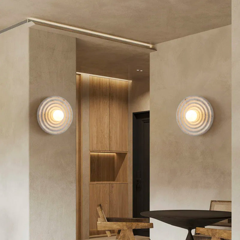 Two circular glass wall lights emit a warm glow against modern beige walls.