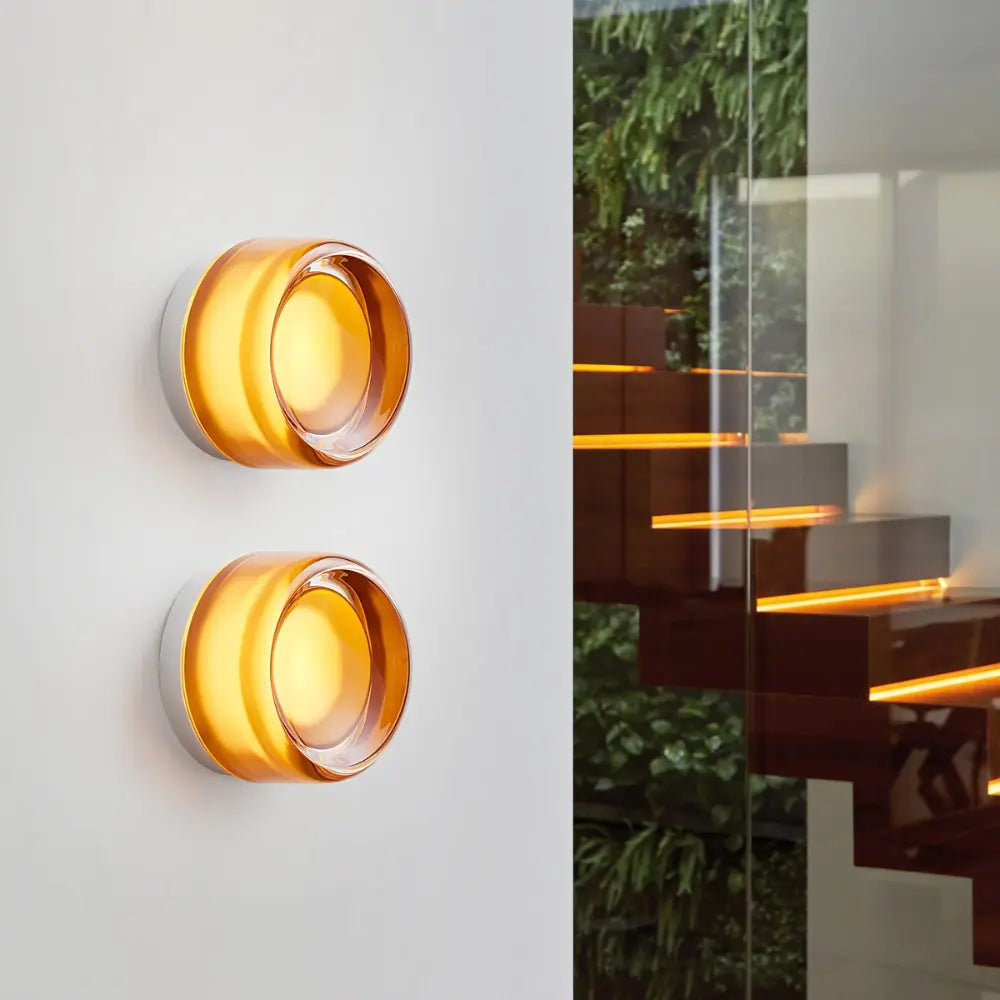 Two round Scandinavian blown glass wall lights mounted on a white wall, softly glowing.