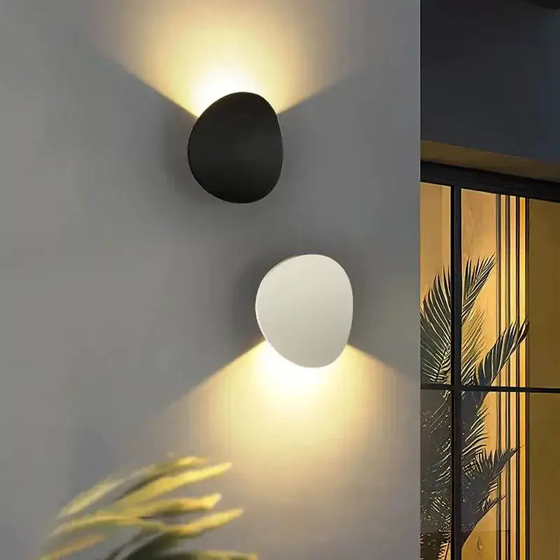 Two round aluminum LED wall lights, one black and one white, emit soft yellow light.