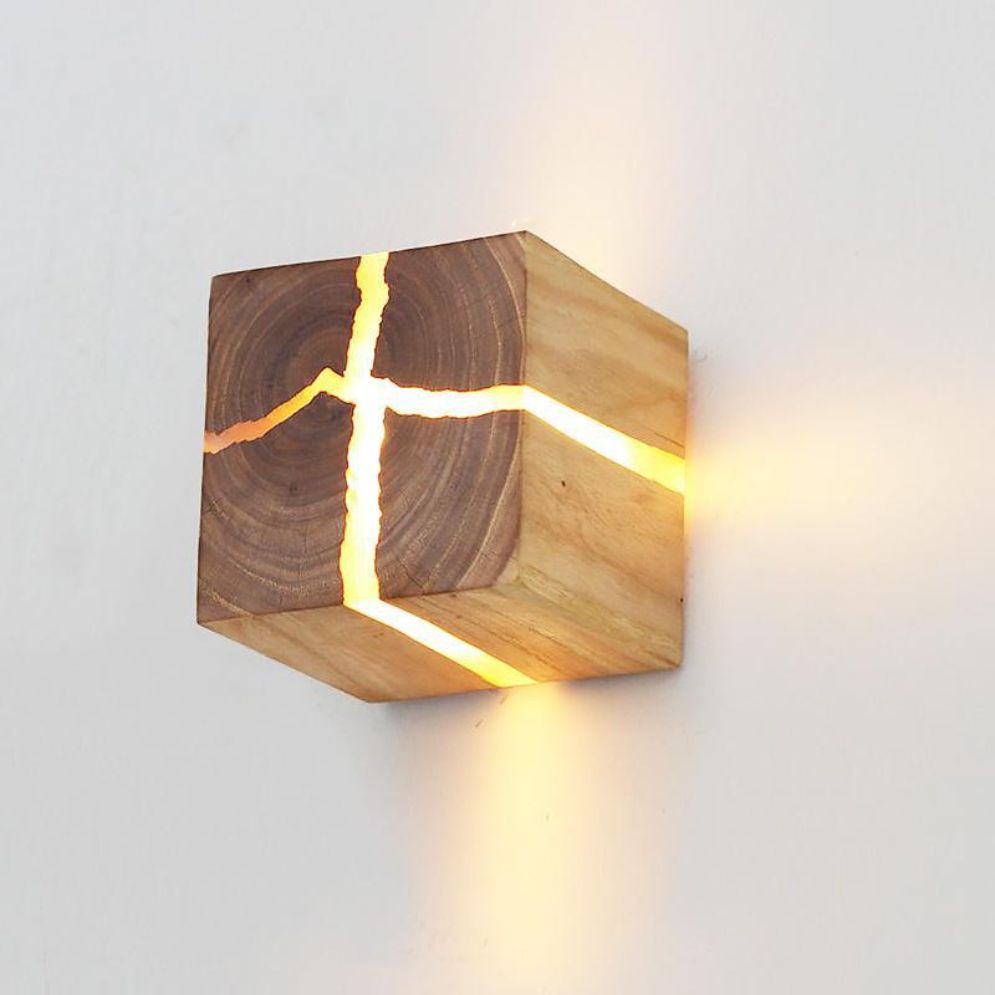 Wooden cube LED wall light with glowing cross-pattern cracks and warm light shining through.