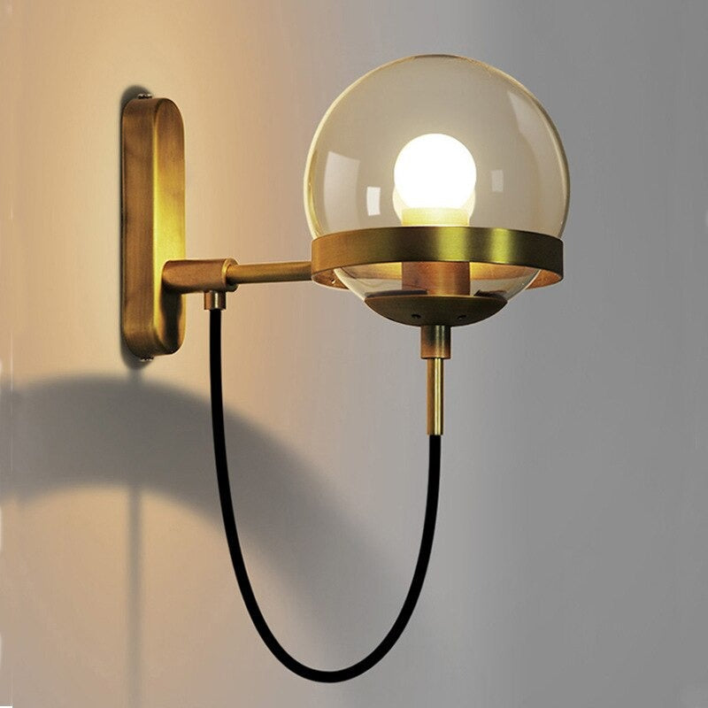 Brass wall light with round glass globe and exposed bulb offers sleek, modern illumination.
