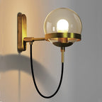 Brass wall light with round glass globe and exposed bulb offers sleek, modern illumination.
