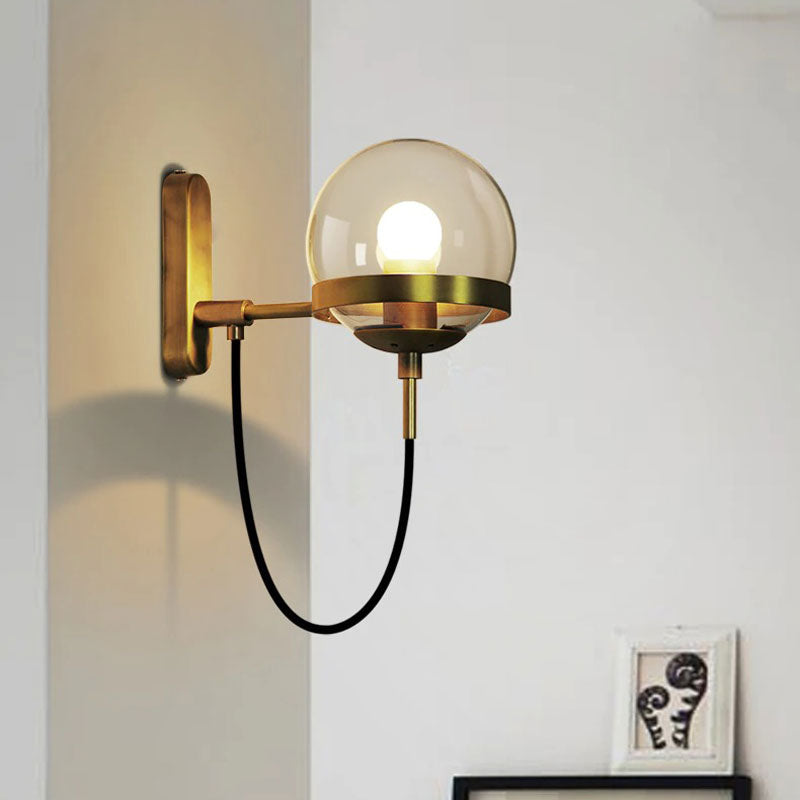 Modern glass globe wall light with clear shade and exposed bulb, radiating stylish illumination.