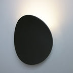 Minimalist black oval LED wall light casts a soft, elegant glow on white walls.