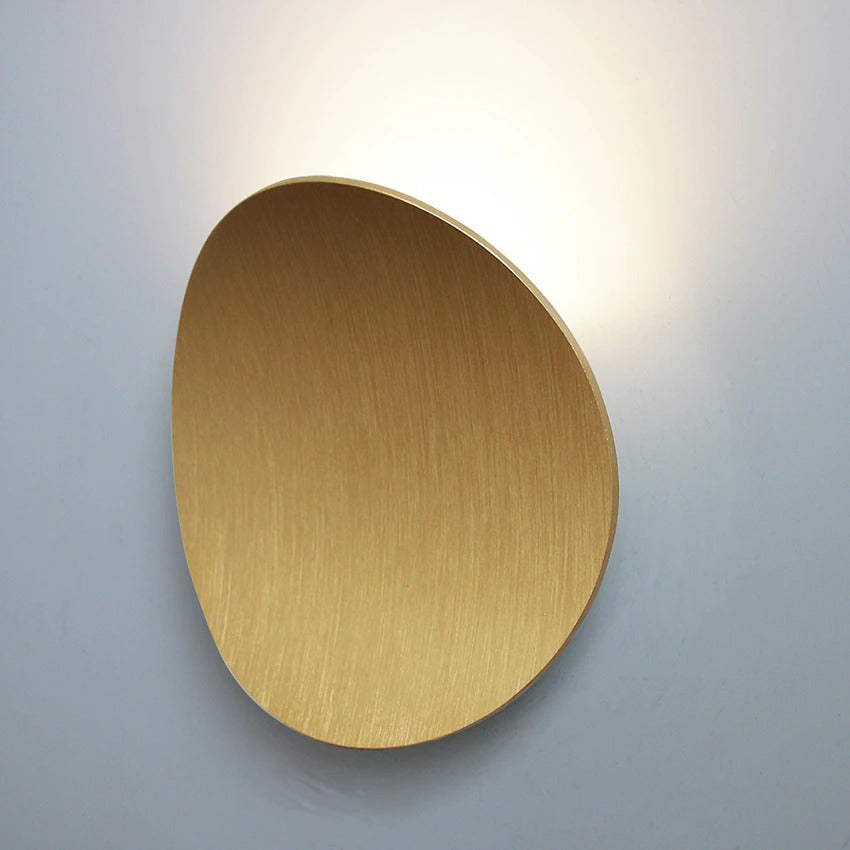 Soft, diffused LED light radiates warmly from a sleek circular brushed gold wall fixture.