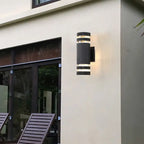 Luminaire LED cylindrique en acier brossé fixé sur un mur crème.