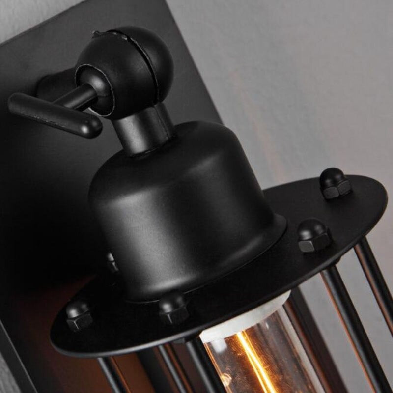 Industrial black iron wall light with exposed screws casts warm glow through clear bulb cover.