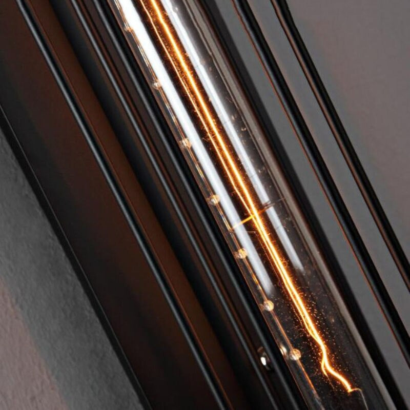 Bright filament glows inside tubular wall light, black metal bars intensify the illumination.