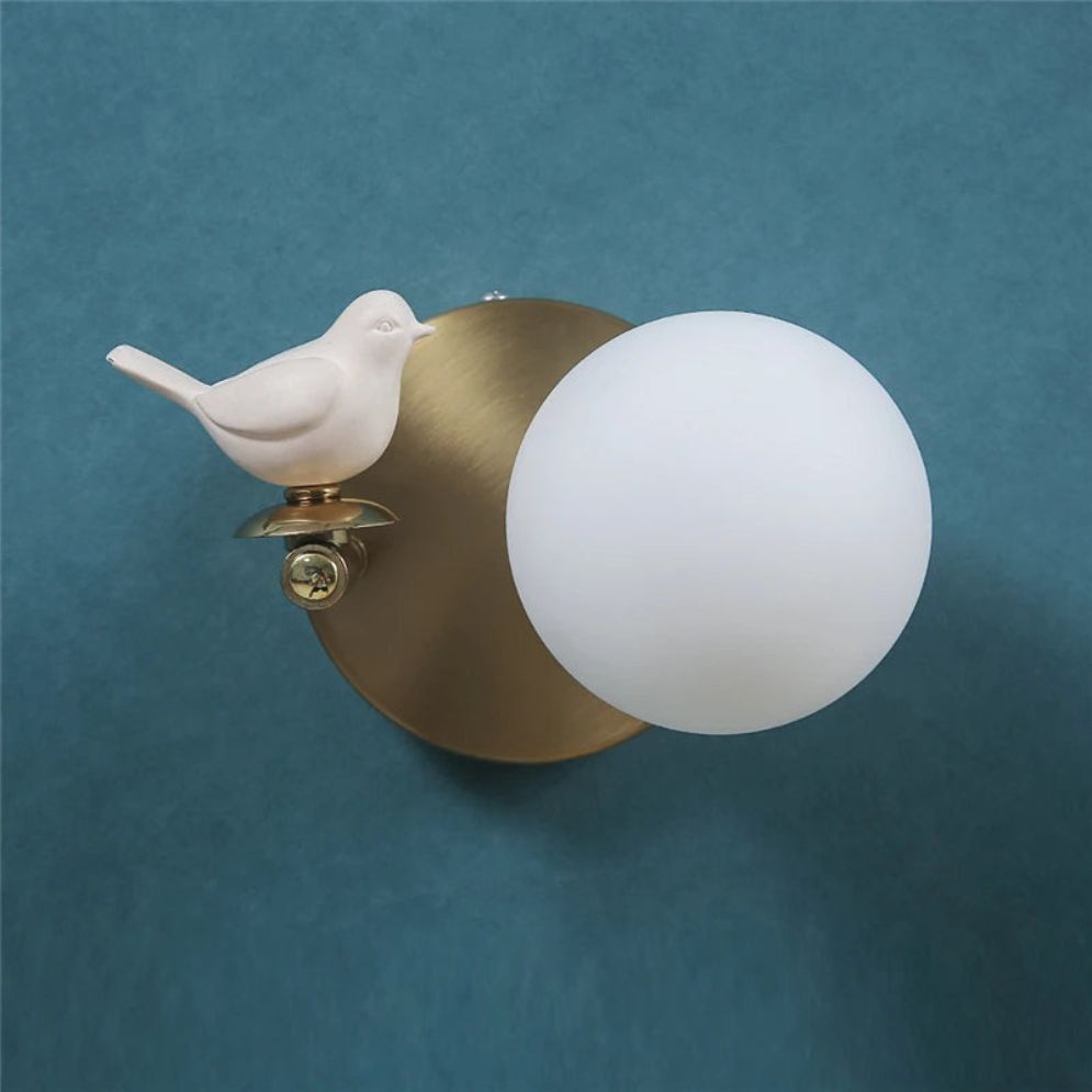 Elegant wall light with brass base, white glass shade, and ceramic bird detail.