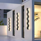 Lampe murale extérieure LED noire au motif ondulé diffusant une lumière chaude.