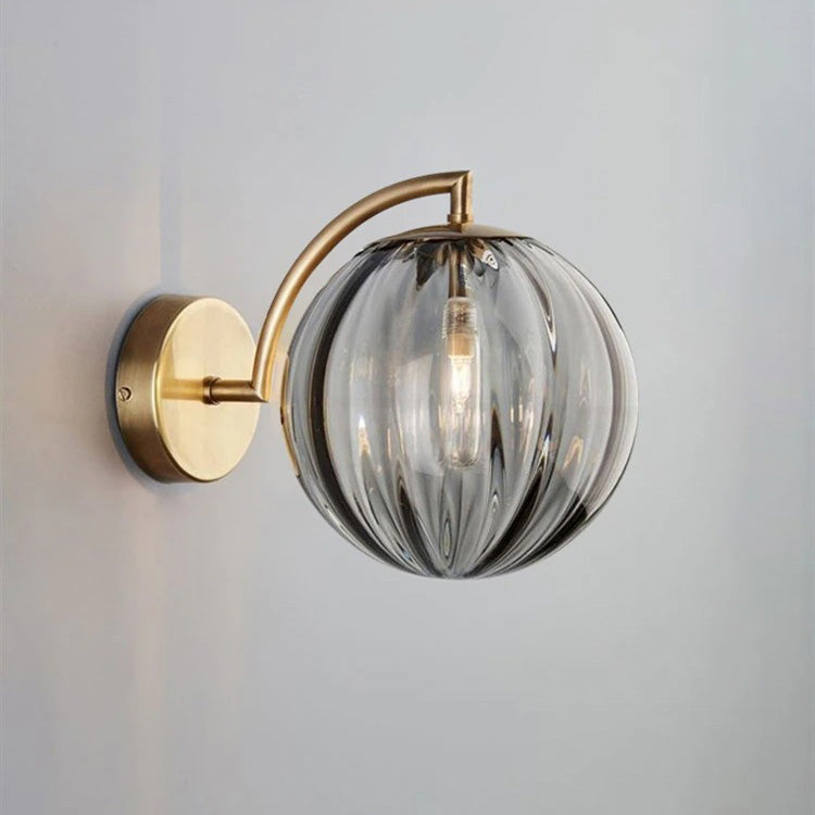 Soft, moody light glows from a smoked glass ball wall lamp with curved brass arm.