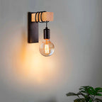 Warm exposed bulb glows against a gray wall in a modern black sconce.