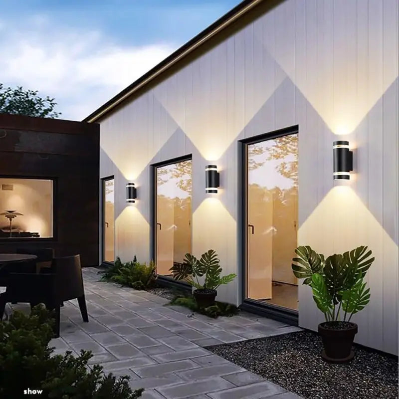 Trois appliques cylindriques noires projettent des éclats lumineux chauds en losange sur un mur blanc.