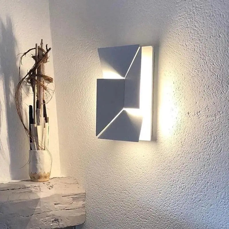 La Maison Applique murale en fer blanc diffuse une lumière douce sur le mur texturé.