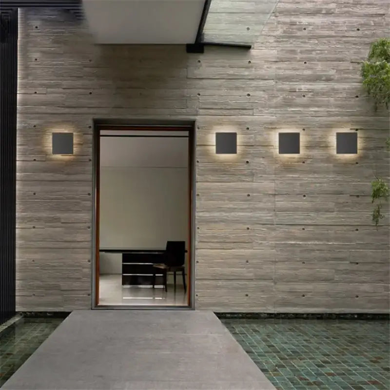 Trois appliques murales design carrées en aluminium LUMINAIRE MAISON extérieures alignées sur le mur.