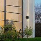 Applique murale LED aluminium moderne, lumière verticale chaude éclaire une façade blanche.