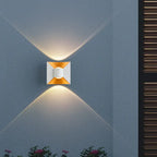 Applique murale extérieur noir incurvé diffusant une lumière LED chaude en forme de X.