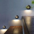 Trois appliques murales rondes en aluminium diffusent une douce lumière LED sur un mur clair.